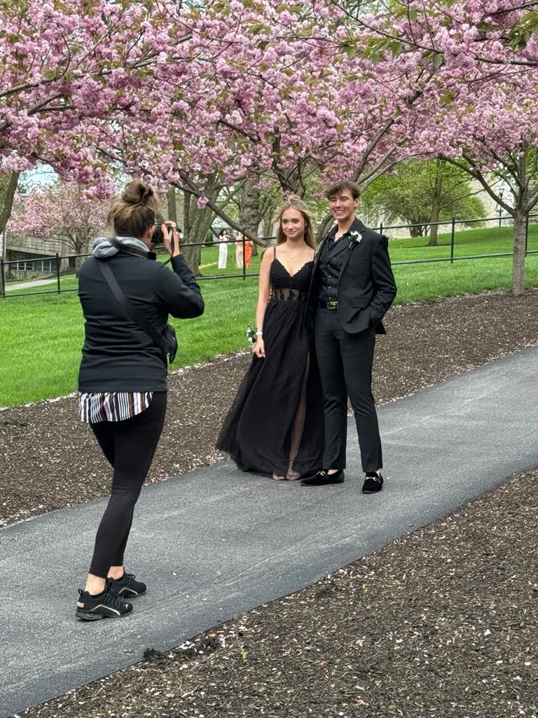 Behind-the-scenes view of photographer shooting prom couple under pink cherry blossom trees in park