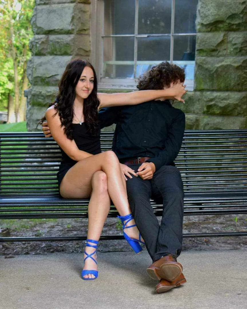 Two young people on park bench, playfully pushing companion's face