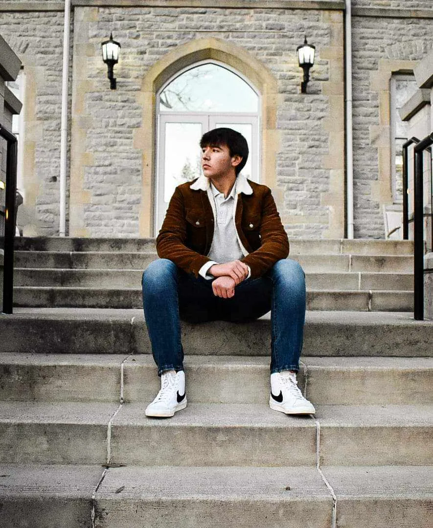 Young man sits contemplatively on stone steps wearing brown sherpa jacket
